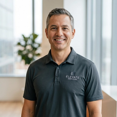 David R., a service business owner, smiling in a bright office while wearing an Elevate Services polo shirt