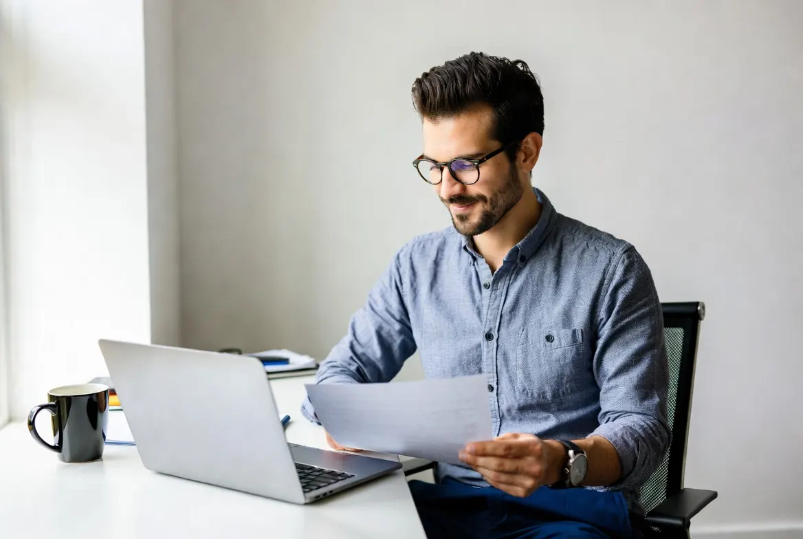 Small business owner reviewing a credit card processing statement at a desk with a laptop, considering a payment processing rate audit