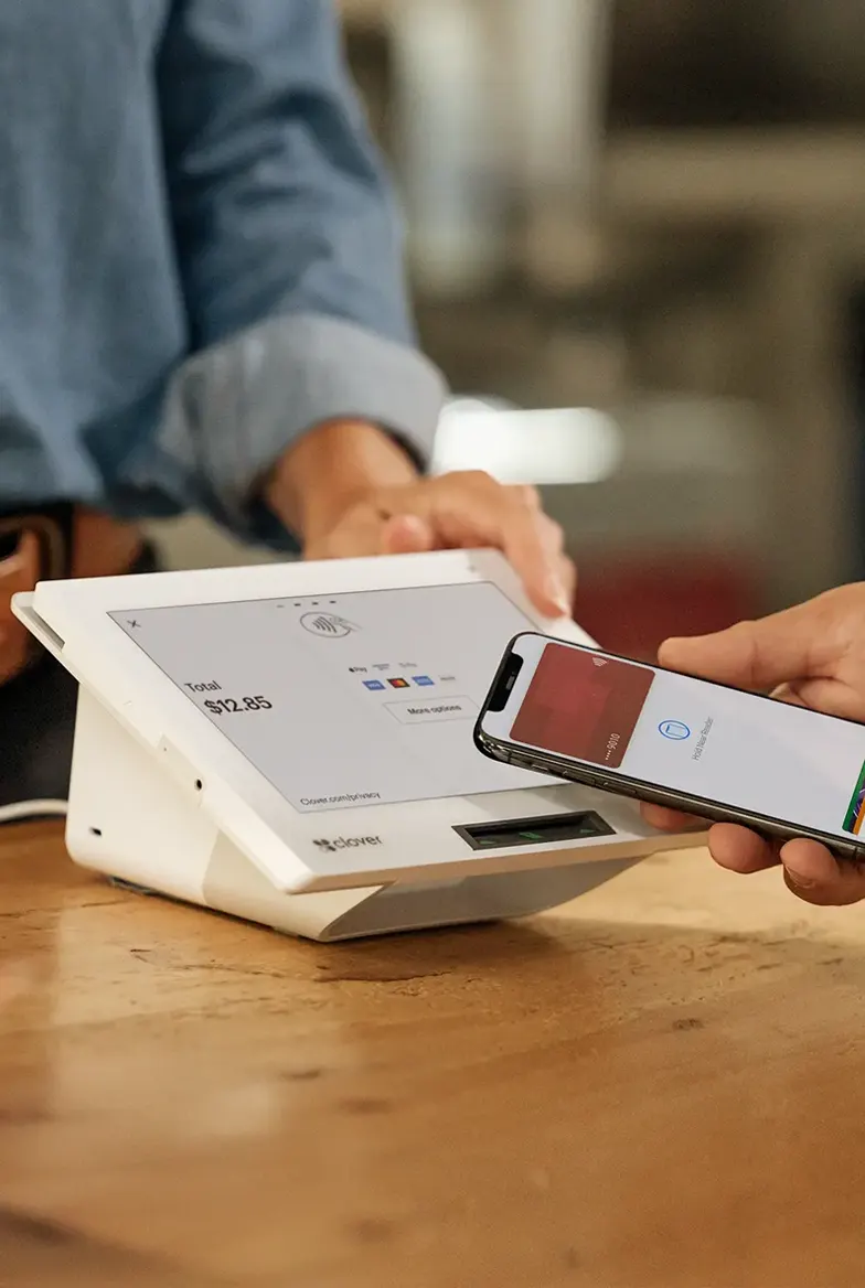Customer completing a contactless tap-to-pay transaction on a Clover countertop POS terminal showing a checkout total