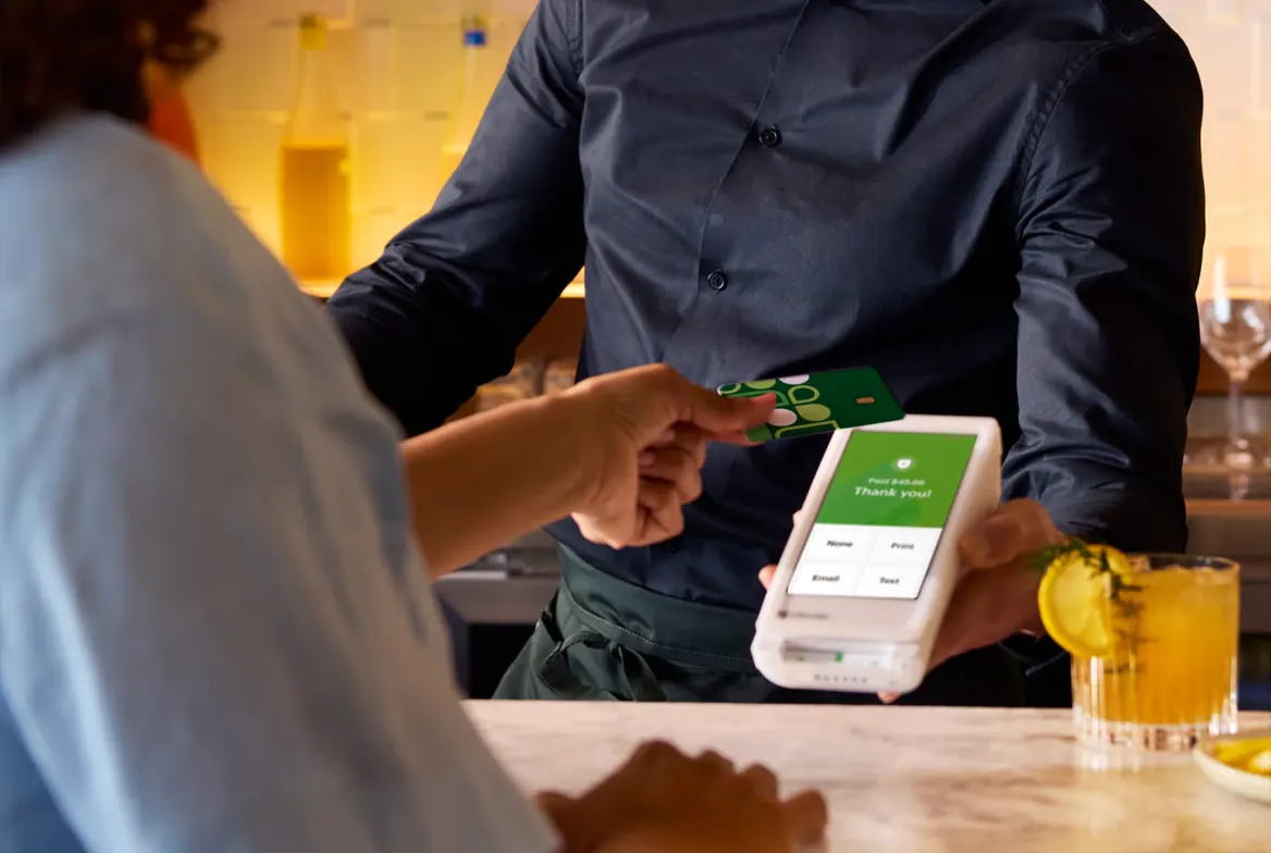 Restaurant server accepting a contactless card payment at a dining table using a mobile smart terminal.