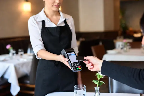 Restaurant server using a handheld mobile terminal to take a customer's order and payment at the table.
